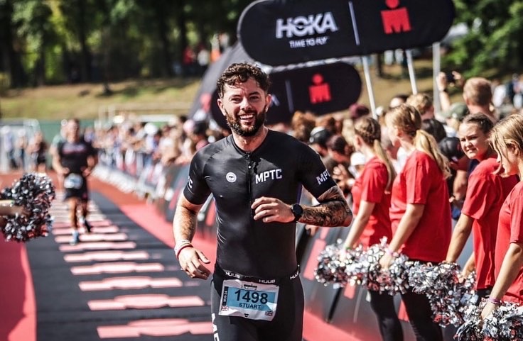 An athlete runs down the finish line of an IRONMAN triathlon with a broad smile across his face