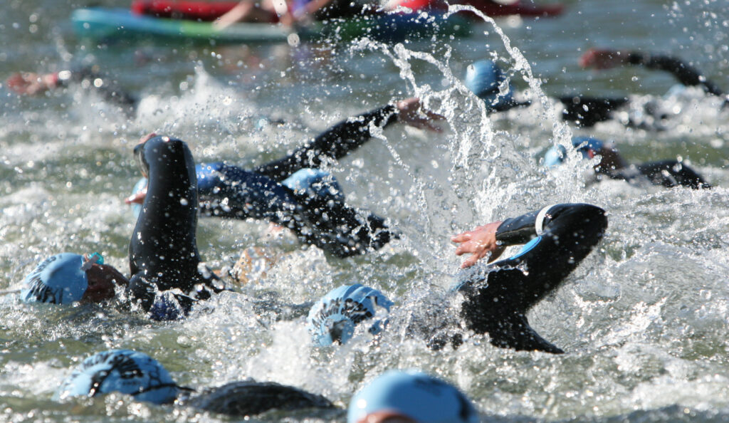 A large group of IRONMAN athletes swim in close proximity to each other