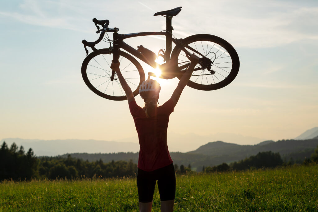 An online coaching client who is a beginner celebrating a successful bike ride by lifting their bike in the air.