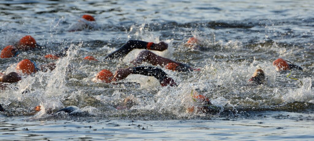 A group of open water swimmers in orange hats taking part in what could be an olympic distance or 70.3 triathlon.