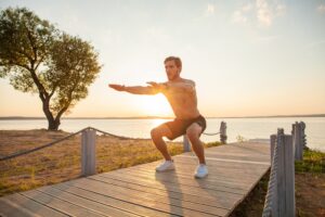 A triathlete perfuming a bodyweight squat on a pier against the sunset to get stronger and help prevent triathlon injuries