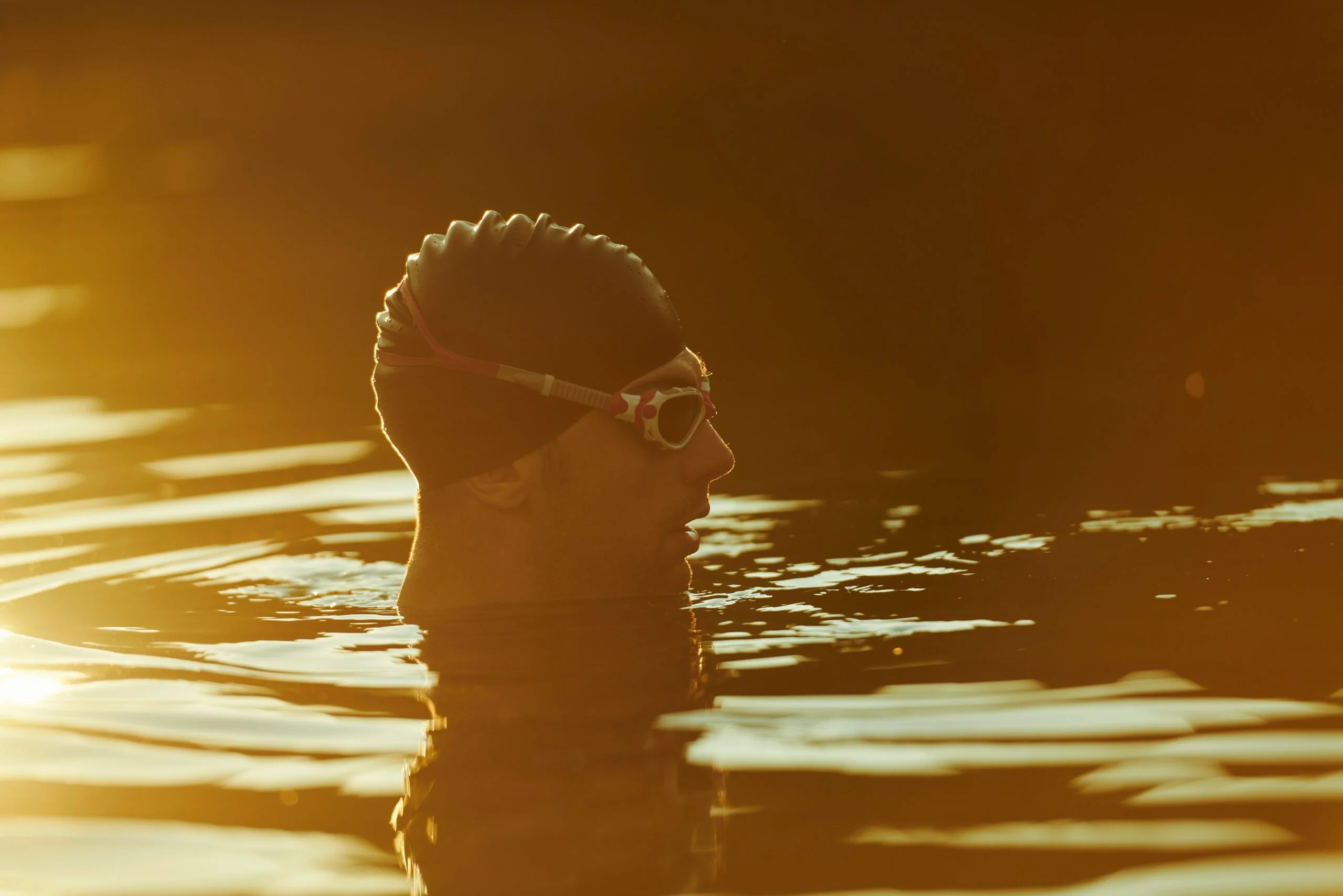 A swimmer following an online triathlon coaching programme, resting during golden hour during a lake swim.